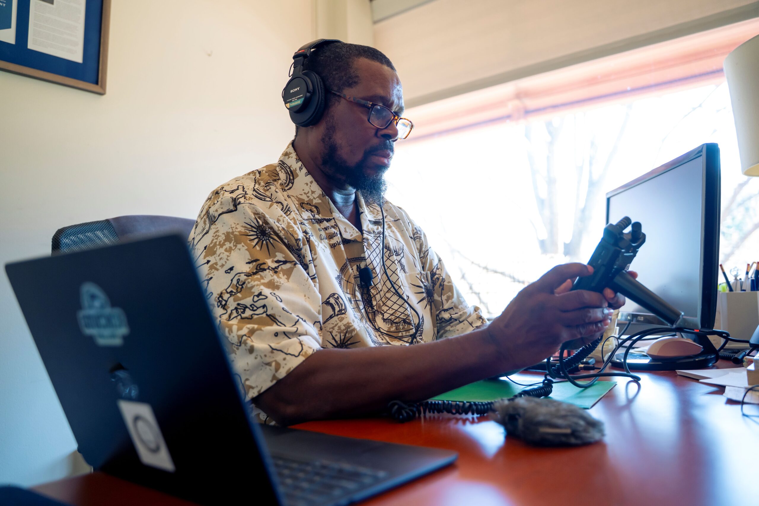 Man at desk with headphones on and audio recorder