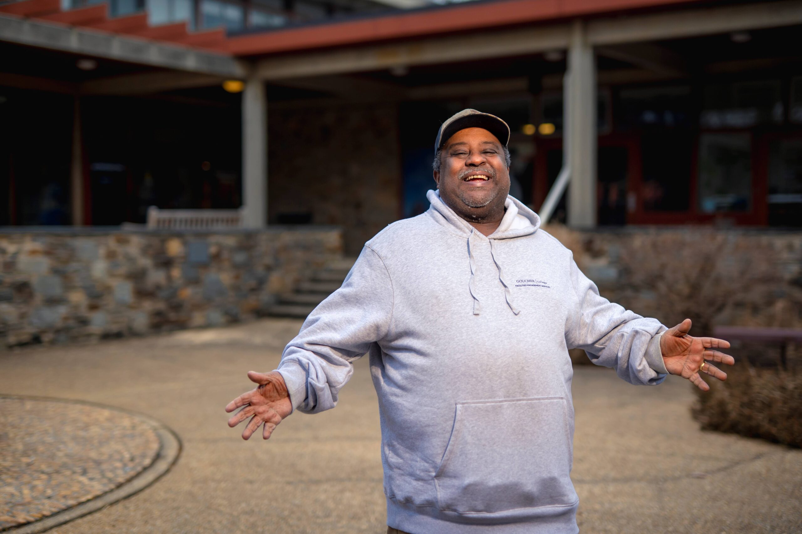 Ray West stands in Dorsey Courtyard smiling with his arms oustretched