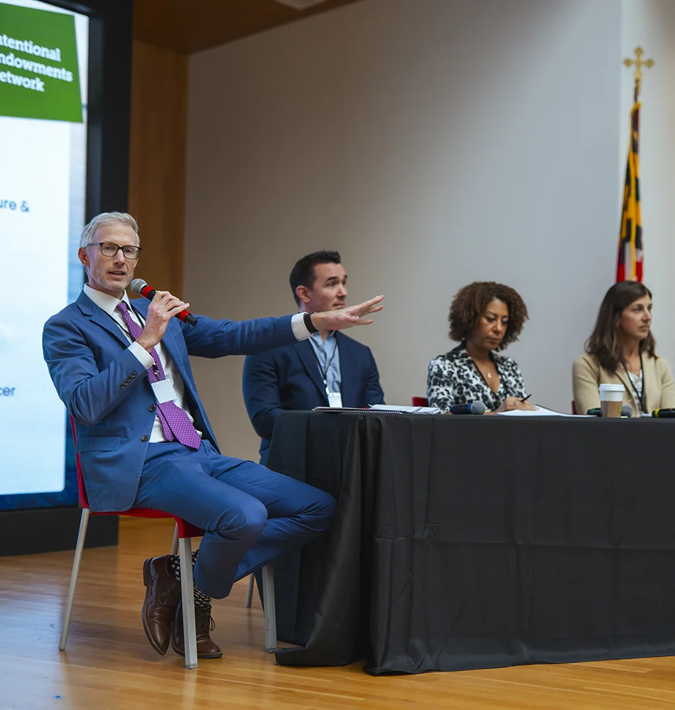 A panel sits on a stage speaking to the audience at the Intentional Endowment Network Forum hosted at Goucher College Athenaeum