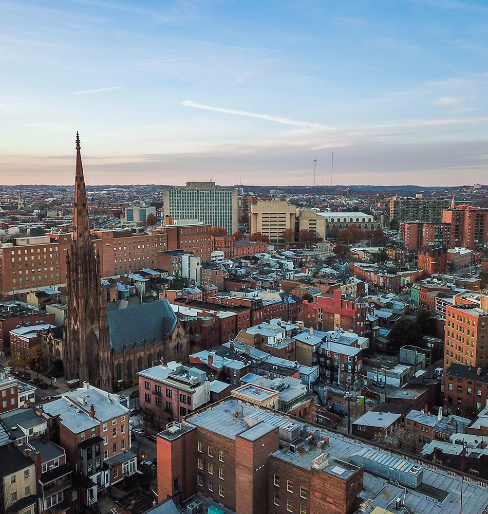 A sweeping landscape photograph of Baltimore City with a calm sunset in the background.